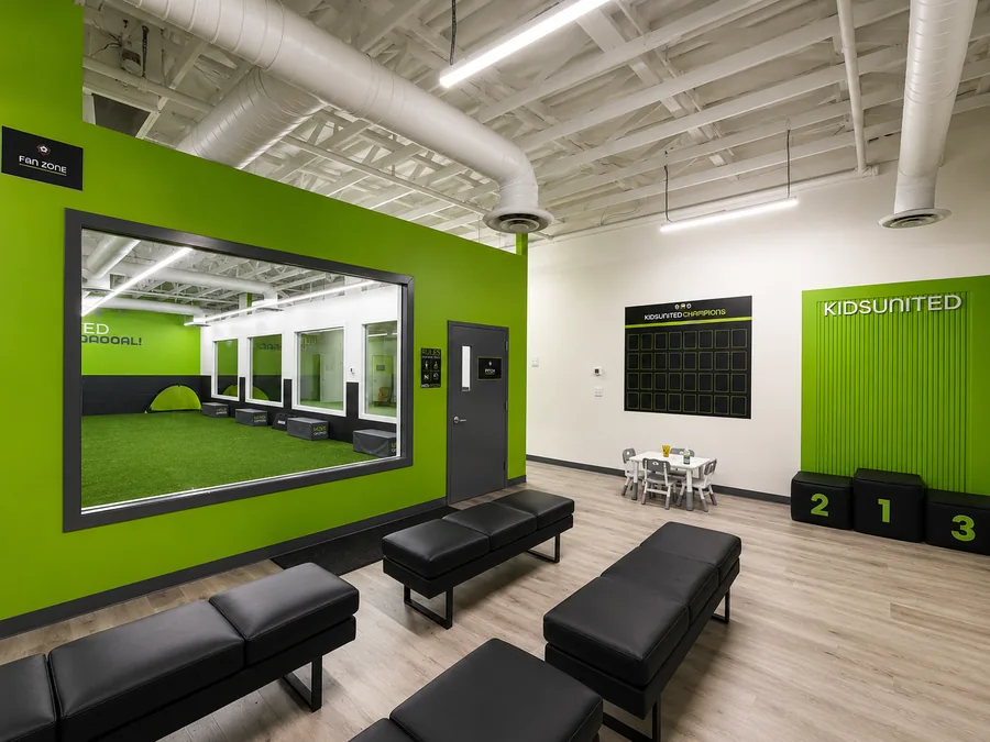Kids United Sports Gym: Alternate waiting area with benches, green dividing wall, viewing windows, and branded podium