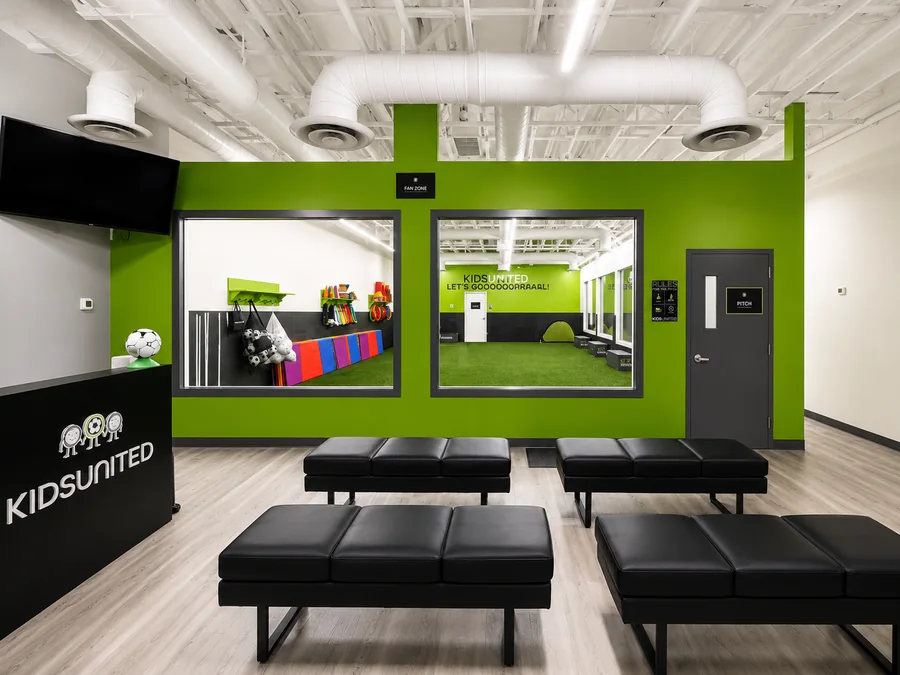 Kids United Sports Gym: Frontal finished reception desk, spectator seating and windows into gym